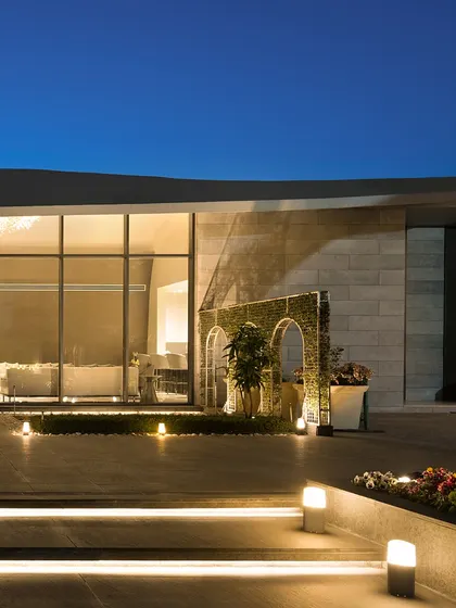 The transition from the landscaped steps to the interior of "The Rising Wave" is illuminated by subtle ground lighting. This guides the eye towards the floor-to-ceiling glass, blurring the line between inside and out.