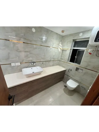 A clean and modern bathroom with a floating vanity and a wall-mounted toilet. The light-colored tiles and gold-toned accents create a bright and elegant space.
