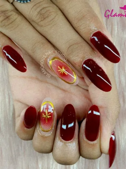 Deep, glossy red nails are paired with a stunning accent nail featuring a golden starburst on a red-to-nude ombré base. This look is the perfect combination of classic elegance and modern art.
