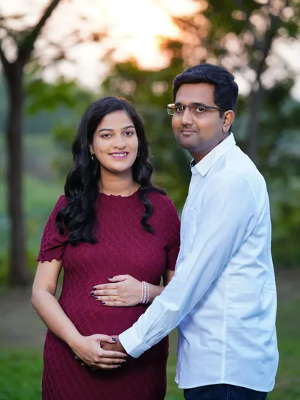 A lovely portrait of an expecting couple in a park at sunset. The warm, golden light of the late afternoon creates a soft and romantic atmosphere.