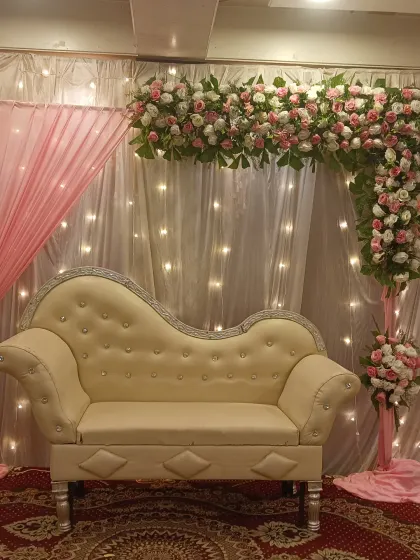 A romantic stage setup perfect for an engagement or reception. We designed an L-shaped floral arch with pink and white roses over a white chaise lounge, complemented by soft pink and white drapes with fairy lights for a warm glow.