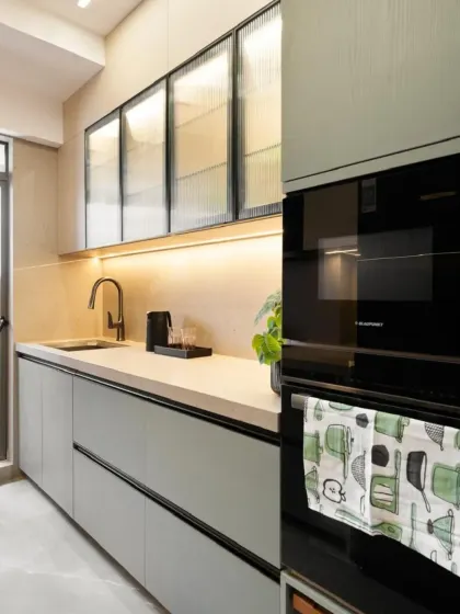 This kitchen features an integrated oven and fluted glass upper cabinets, which add texture while partially obscuring the contents. The warm under-cabinet lighting highlights the clean lines and matte finish of the lower cabinets.
