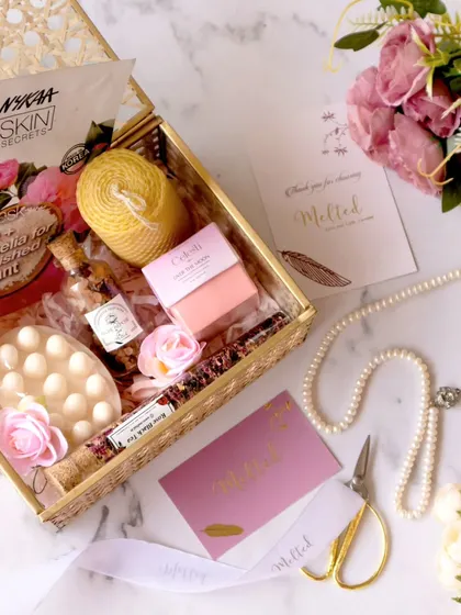 An overhead shot of a curated gift box, complete with a Nykaa skin secrets mask, pearls, and floral elements. The composition is a beautiful blend of textures and soft colors, creating a luxurious feel.