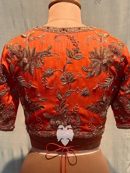 The back of an orange raw silk blouse, covered in golden floral details.