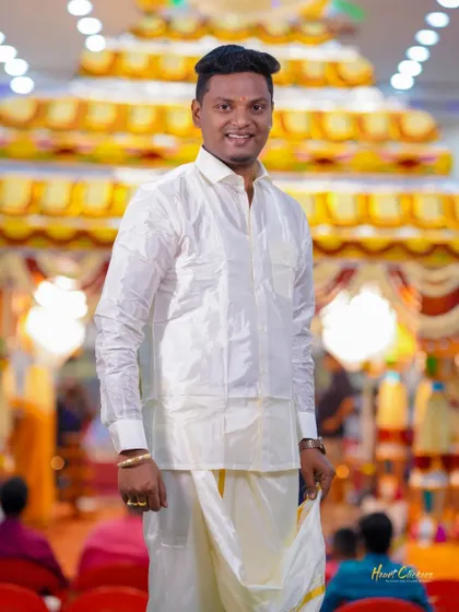 A portrait of the groom in traditional attire, standing in a brightly lit wedding hall.