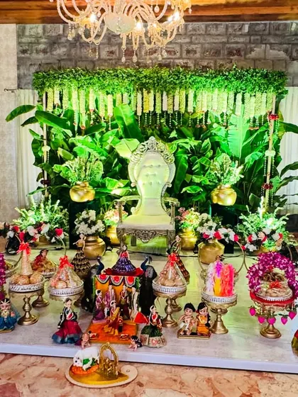 A stunning platter display for a function with a lush green backdrop. The combination of traditional dolls, ornate platters, and a grand chandelier creates a truly luxurious feel.