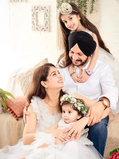 A playful and loving family portrait, with the older daughter giving her dad a hug from behind.