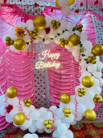 A beautiful birthday balloon ring in white and gold, set against a pink curtain backdrop.