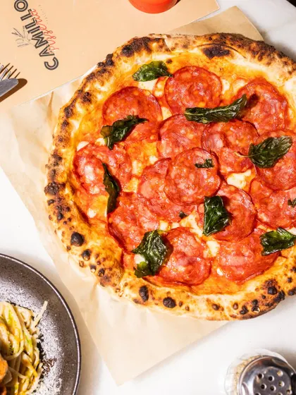A top-down view of my classic Pepperoni pizza, generously topped with spicy pepperoni and fresh basil leaves. The pepperoni crisps up beautifully in the wood-fired oven, its flavor infusing the entire pie. A true crowd-pleaser.