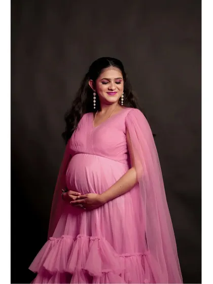 A close-up look at the delicate details of the pink tiered ruffle maternity gown. The V-neck and sheer cape sleeves are designed to be flattering and comfortable for expecting mothers.