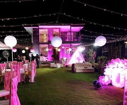 A wide view of the outdoor first birthday party venue, showing the guest seating, tents, and the main decoration area lit up in pink.