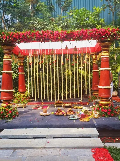 A stone pathway lined with red flower petals leading to a traditional red-pillared mandap.
