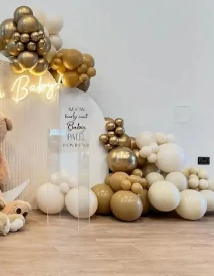 An elegant baby shower setup with an 'Oh Baby' neon sign, chrome gold and neutral balloons, and plush teddy bears.