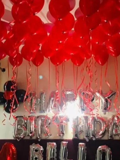 A classic birthday room setup using red and black balloons to cover the ceiling. The silver 'HAPPY BIRTHDAY' foil letters stand out and create a festive focal point in the room.