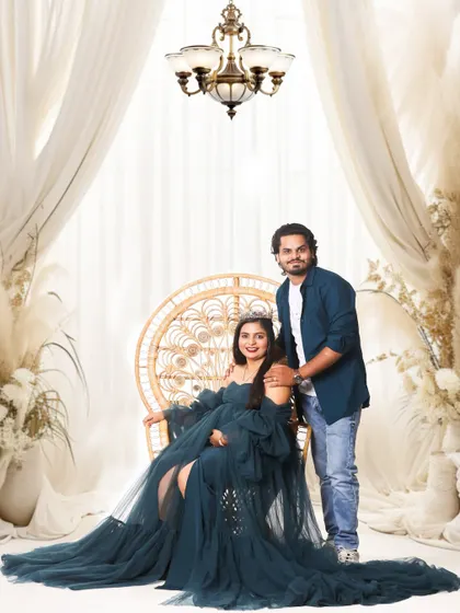 A regal studio portrait featuring an elegant chandelier and flowing drapes. The mother-to-be looks radiant in a dark teal gown, creating a sophisticated and classic maternity photo.