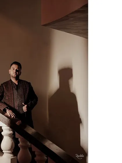 Another shot of the groom's Sangeet look, capturing the intricate details and rich texture of his embroidered jacket under dramatic lighting.