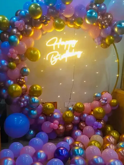 A vibrant birthday party decoration with a full ring of purple, pink, and gold balloons.