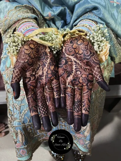 The deep, mature stain of a full-palm floral design, beautifully accessorized with floral bracelets for a wedding ceremony.