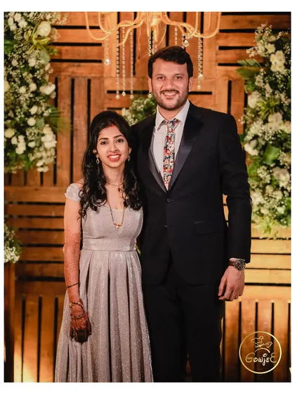 A happy couple posing against a rustic wooden pallet wall decorated with white flowers.