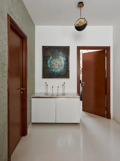 This view shows the passage leading from the dining area, featuring a simple white console table and contemporary Islamic art. The pendant light adds a touch of modern elegance to the space.