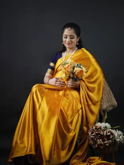 A graceful portrait of an expecting mother in a shining yellow satin saree. This studio shot captures a quiet moment of reflection and anticipation.