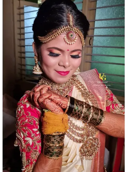 The final touches for Shruthi's muhurtham look. The warm, golden-orange eyeshadow complements her off-white and red silk saree beautifully.