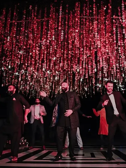 The groom's crew takes over the dance floor under a ceiling of shimmering red sequins, bringing the energy for the Sangeet night.
