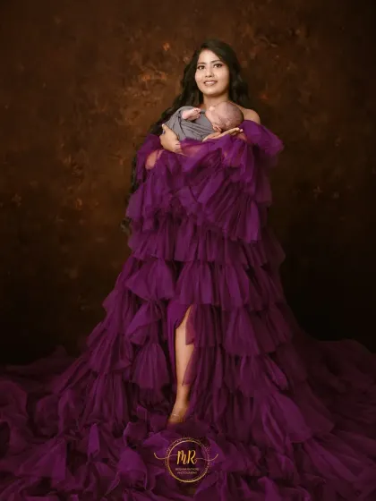 A full-length portrait showing the dramatic scale of the ruffled purple gown as the mother holds her newborn. This is a true statement piece of art.