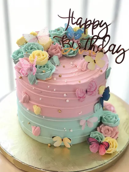 A pastel dream, this cake features a pink and blue ombre design, buttercream roses, and a flutter of colorful butterflies.