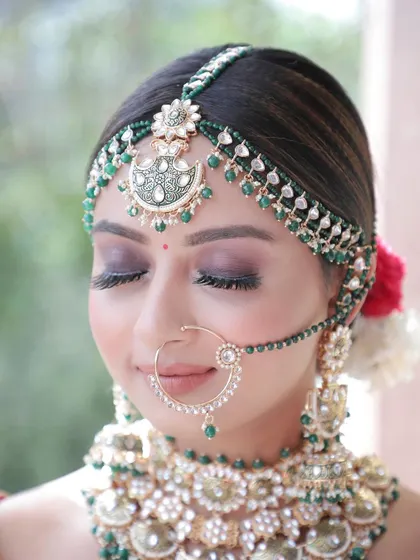 A detailed close-up shot focusing on the bride's stunning makeup and jewelry. This type of shot highlights the incredible artistry involved in creating the perfect bridal look, from the eye makeup to the intricate nath and maang tikka.