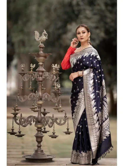 A regal portrait featuring a dark navy blue Banarasi silk saree. The outdoor setting with a traditional brass lamp adds a cultural and timeless context to this ethnic fashion photograph.
