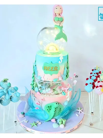 Here is one of my favorite mermaid-themed dessert tables. The centerpiece is a stunning three-tiered cake with an illuminated globe, surrounded by matching under-the-sea cakepops. I can create a complete, coordinated look for your event.
