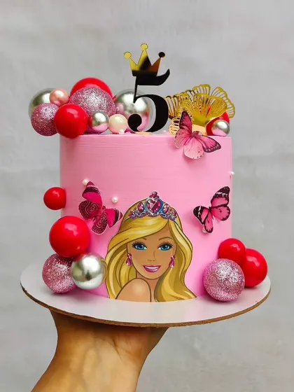 This Barbie cake is all about pink and glitter. It's decorated with red and silver spheres, butterfly accents, and a crown for a truly royal fifth birthday.
