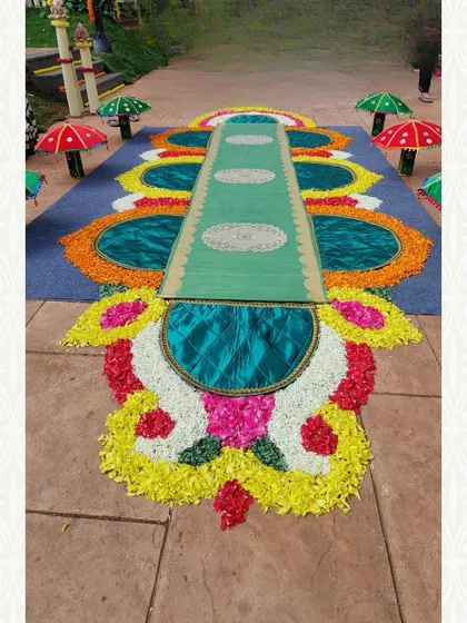 A traditional floor decoration using silk fabric and flower petals. The small decorative umbrellas add a touch of whimsy and color to the arrangement.