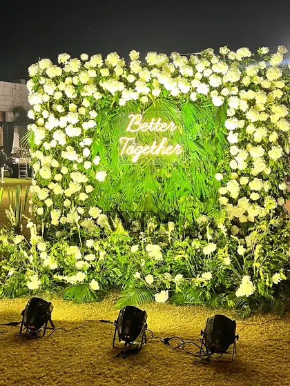 A beautiful and lush photo wall. A frame of white flowers surrounds a green backdrop with a 'Better Together' neon sign, creating a perfect spot for couple and guest photos.