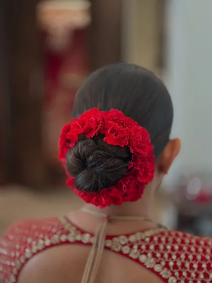 A clean and classic bridal juda, beautifully encircled with a vibrant red floral gajra. This is a signature look for the main wedding day, designed to perfectly complement a traditional red lehenga.