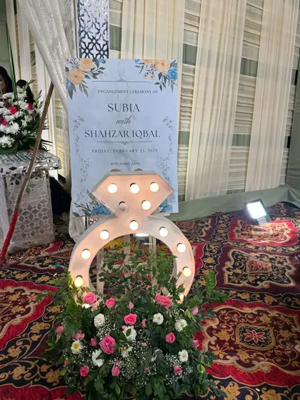 A unique decor element for an engagement party. A large, lit-up marquee in the shape of a diamond ring stands next to the personalized welcome sign.