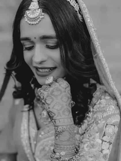 A candid black and white shot of the bride smiling. This captures a moment of genuine happiness and shyness, showing her beautiful henna-adorned hand.