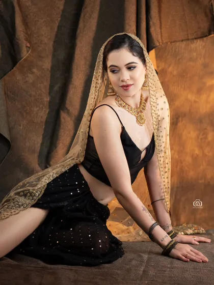 A relaxed, seated pose in a modern fusion outfit. The combination of a contemporary top with a traditional draped skirt and dupatta creates a unique and stylish look.