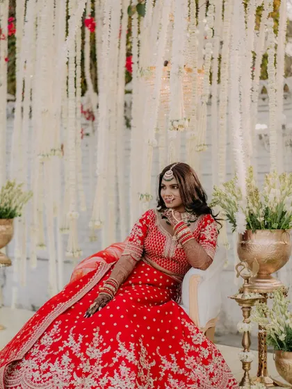 Another beautiful portrait showing the bride's radiant smile. The combination of her red lehenga, glam makeup, and the stunning decor creates a truly magical image.