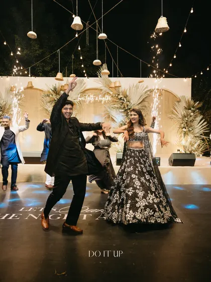 A high-energy moment from the sangeet night, with the couple dancing under a sky of hanging bells and string lights. The stage is set for a night of pure celebration.