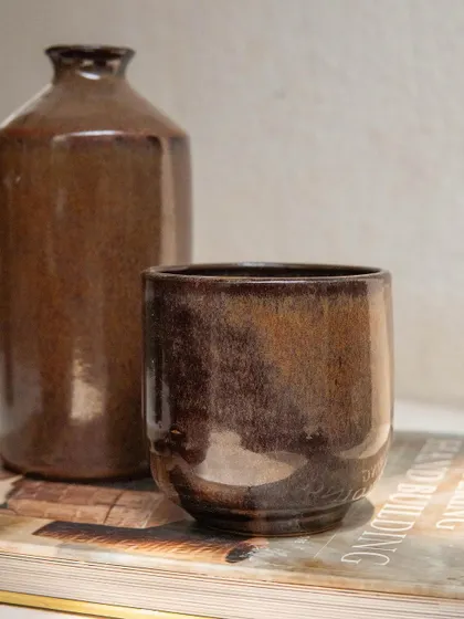 The Copper Patina glaze seen here on a cup and bottle form. Its reddish orange pooling effect adds character and depth to each piece.