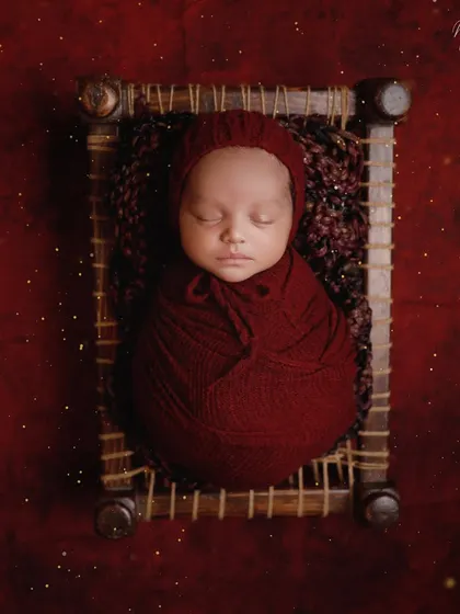 A touch of tradition with this miniature charpai. The rich red wrap and background create a warm and vibrant portrait, celebrating our cultural roots.