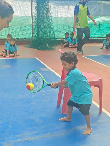 A coach provides encouragement as a young student makes contact with the ball. Our hands-on approach ensures every child gets the attention they need to develop proper tennis technique from an early age.