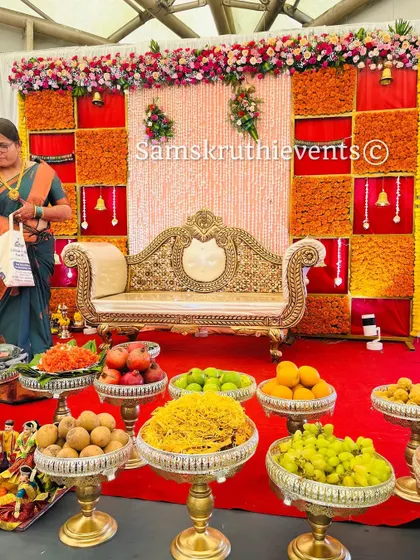 A simple yet elegant baby shower setup. The focus is on the beautiful arrangement of fresh fruits and sweets on silver stands, set against a traditional backdrop.