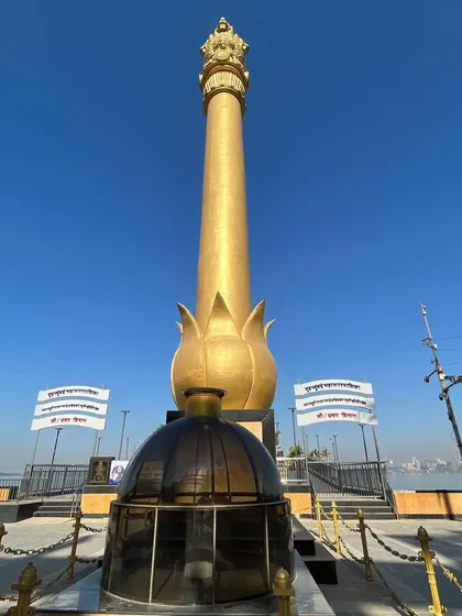 The golden Ashoka pillar monument at Chaitya Bhoomi in Dadar, standing tall against a bright blue sky.