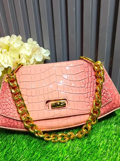 This pink bag with a crocodile skin texture and a chunky gold chain strap is a trendy, high-fashion accessory to complete your look.