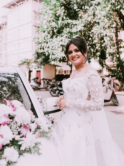 The bride arriving in style. Her smile is radiant as she poses by the wedding car, ready for her big day.