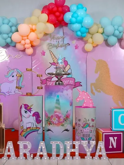 A dreamy unicorn-themed first birthday party. The decor is filled with pastel rainbow colors, unicorn illustrations, and soft, cloud-like balloons to create a whimsical and magical atmosphere for the celebration.