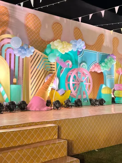 The stage for our 'Candyland' party, featuring giant ice cream cones, macarons, and a ferris wheel, all in sweet pastel shades.